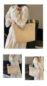 Detail of large beige woven straw tote bag featuring soft cotton rope handles and pom-poms