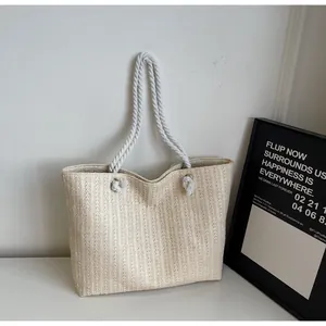 Detail of hand-woven beige straw tote with thick white rope handles and silver metal rings