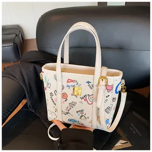 Detail der weißen Graffiti-Tasche mit bunten Handzeichnungen und goldenem Metall-Logo