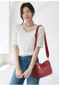 Detail of dark red lychee grain leather crossbody bag with golden kangaroo logo and zippers