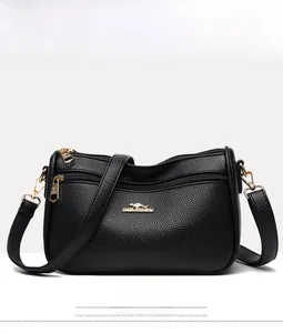 Front detail of black pebble leather crossbody bag with gold logo and zipper pockets