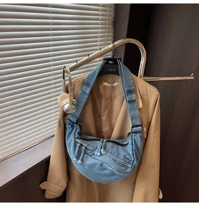 Detail of blue denim crescent crossbody bag with multiple zip pockets and frayed tassels