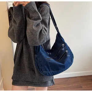 Detail of blue denim hobo bag showing front diagonal zipper pockets and washed texture