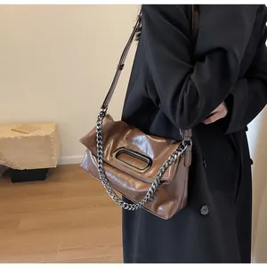 Detail der braunen Kunstledertasche mit ovaler Silberschnalle und klobiger Metallkette