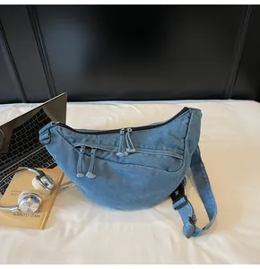 Detail of blue denim crescent crossbody bag with double zippers and adjustable strap