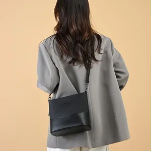 Black leather bucket bag with gold kangaroo logo shown on a model in a grey suit