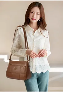 Brown lychee grain leather crossbody bag with kangaroo logo shown on model with lace shirt