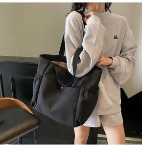 Detail of black canvas tote bag showing elastic side pockets and metal snap button closure
