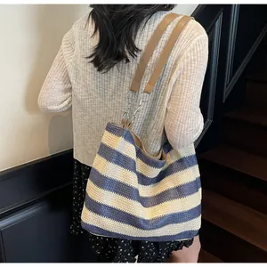 Detail of striped woven tote bag with brown leather straps and silver chain accents
