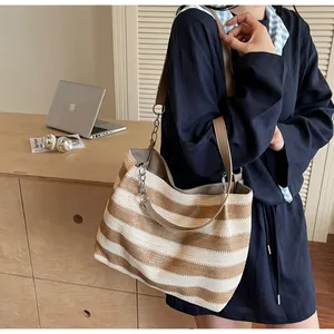 Close-up of woven straw tote bag featuring brown stripes and metal chain shoulder strap