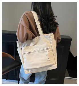Sac fourre-tout en toile beige avec poche zippée et gland, porté sur l'épaule du modèle