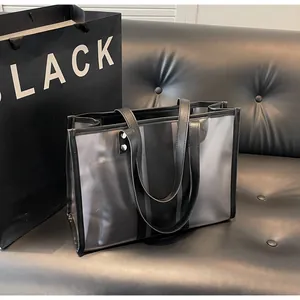 Détail du grand sac cabas transparent rayé avec poignées en cuir sur canapé noir