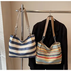 Detail of woven tote bags with colorful stripes, leather straps, and silver chain accents