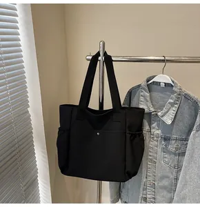 Detail of black nylon tote bag featuring side pockets and snap closure on a metal hanger
