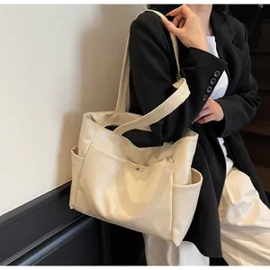 Detail view of large cream tote bag with side pockets on a model in a minimalist setting
