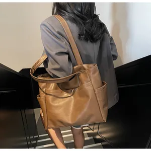 Detail of a large brown leather tote bag featuring a textured finish and metal snap button