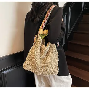 Detail view of large straw tote bag featuring hollow crochet pattern and colorful wide strap