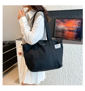 Detail of black canvas tote bag showing magnetic flap pocket and shoulder strap on model