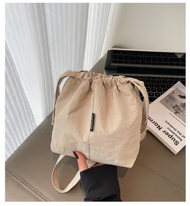 Detalle del bolso de cubo oxford beige con parche de logo negro sobre un escritorio