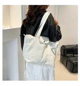 Detail of a large off-white canvas tote bag featuring a side pocket with black button closure