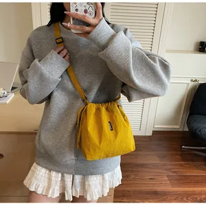 Detalle de bolso cubo amarillo de oxford con cordón, correa negra y etiqueta de logo