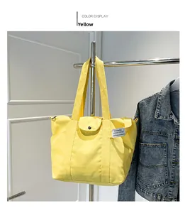 Detail view of yellow canvas tote bag with snap-button flap and side pocket on a hanger