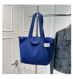 Detail of dark blue canvas tote bag featuring silver snap button and fabric label
