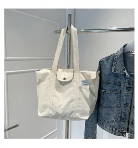 Detail of cream canvas tote bag featuring metal snap button pocket and fashion label