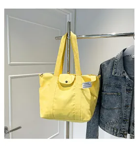 Detail of bright yellow canvas tote bag with wide strap and side pocket hanging on rack