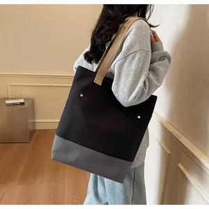 Detail of canvas tote bag with grey-black patchwork and brown fabric straps on a model