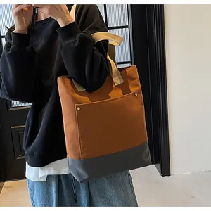 Detail of a large canvas tote bag showing two-tone stitching and golden rivet pocket detail
