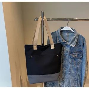 Detail of canvas tote bag showing black fabric, front pocket, and metal rivets close-up