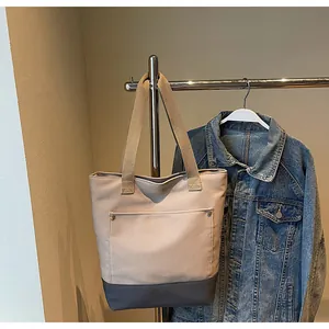 Detail of canvas tote bag showing beige and grey contrast stitching and wide shoulder strap
