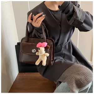 Close-up of a dark brown glossy PU leather handbag with a plush puppy charm and silver lock