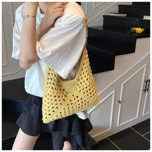 Modelo con un bolso de paja tejido amarillo y asas de cuentas en un ambiente de escalera