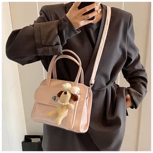 Close-up of pink patent leather handbag featuring a plush dog charm and metal lock closure
