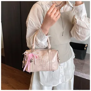 Detail of pink Boston bag featuring embossed logo and pearl ribbon charm accessory