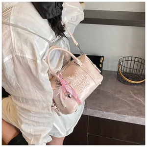 Detail of pink Boston bag featuring embossed letters, bow charm and pearl pendant detail