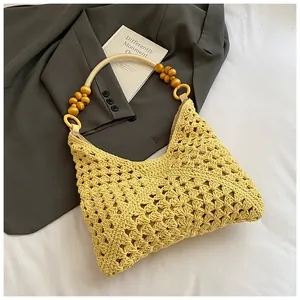 Detalle de bolso tote amarillo tejido a mano con asa de cuentas sobre blazer gris