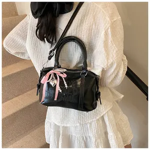 Detail of black glossy Boston bag with pearl charms and bow pendant on white dress