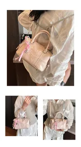 Detail showing pink Boston bag with embossed logo, pearl charm and checkered ribbon bow
