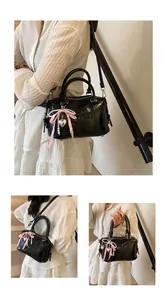 Detail of black glossy Boston bag featuring letter embossing and a pink bow charm pendant