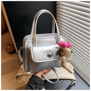 Detail of silver metallic handbag with plush dog charm and luxury turn-lock closure