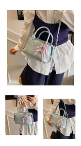 Three views of a light blue Boston bag with embossed letters and a bow charm pendant