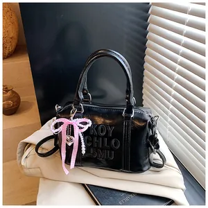 Detail of black patent leather bag featuring debossed letters and a charm accessory