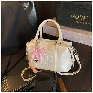 Detail of a creamy Boston bag with embossed letters and pink bow charm with pearls