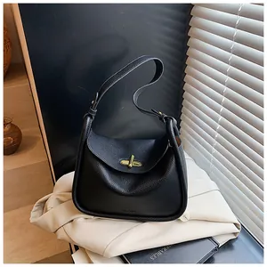 Detail of black lychee grain leather handbag with golden twist lock on beige blazer