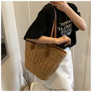 Detailed texture of hand-woven straw tote bag with brown leather shoulder straps