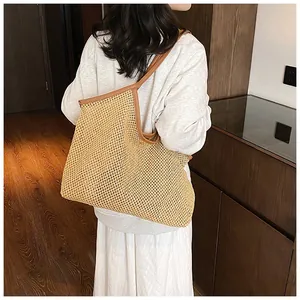 Detail of a large woven straw tote bag with brown leather handles worn by a model