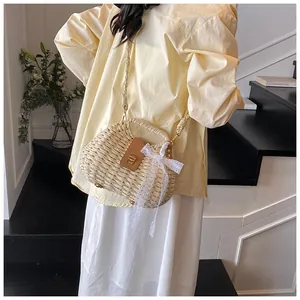 Detail of straw woven beach bag with brown leather flap, metal lock and white lace bow